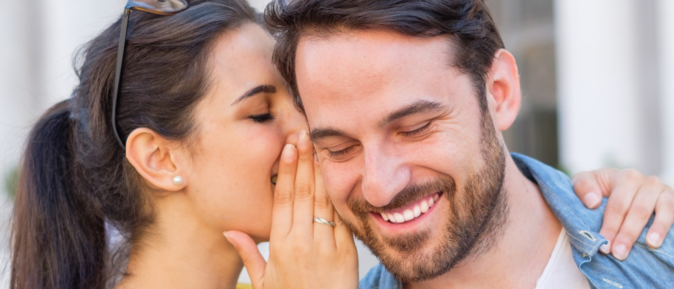 A woman whispering something into her date's ear making him laugh
