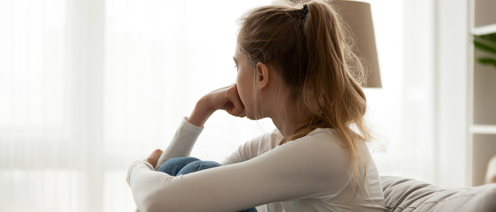 A woman curled up on the couch sadly staring off into the distance