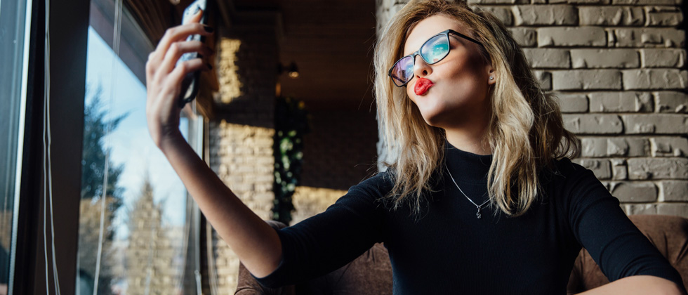 A beautifully made up woman taking duck face selfies with her phone