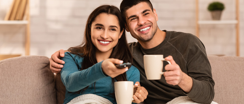 A couple sitting on the couch together turning on a movie