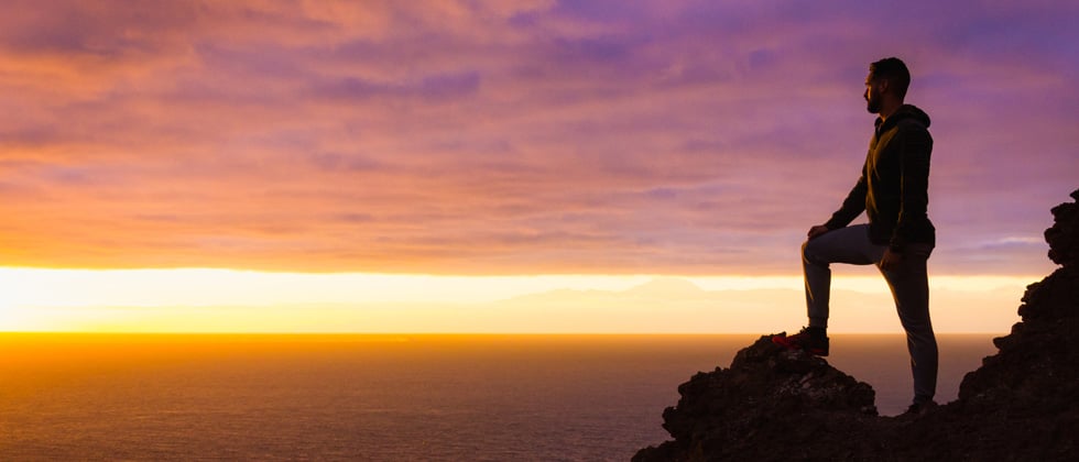 Man standing on top of a mountain at sunrise after a hike