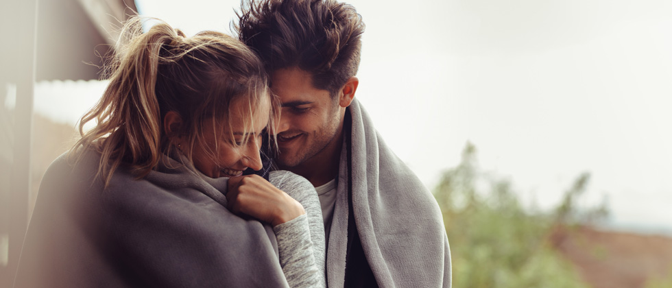 A man and woman cuddling underneath a blanket together
