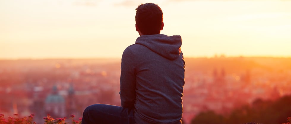 Young guy at the top of a sunset hike looking out to the city
