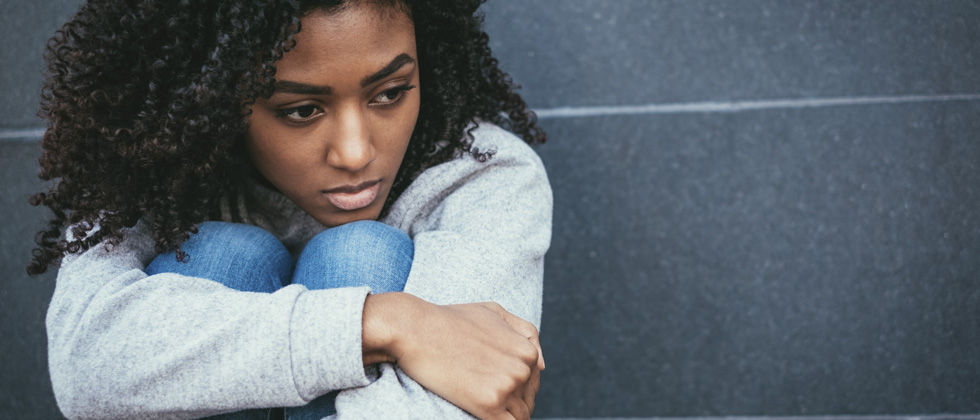 Woman sitting holding her knees to her chin deep in thought