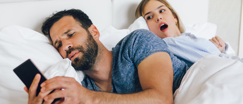 Couple in bed, one texting someone else and the other can see