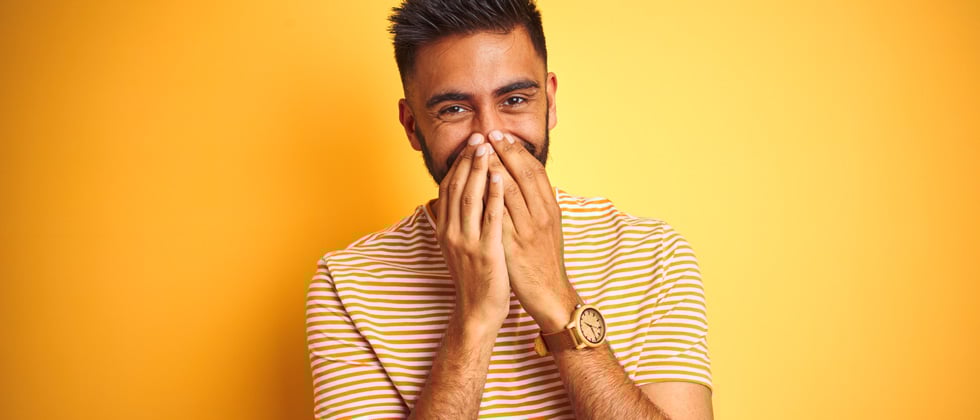 A man holding his hands over his mouth giggling
