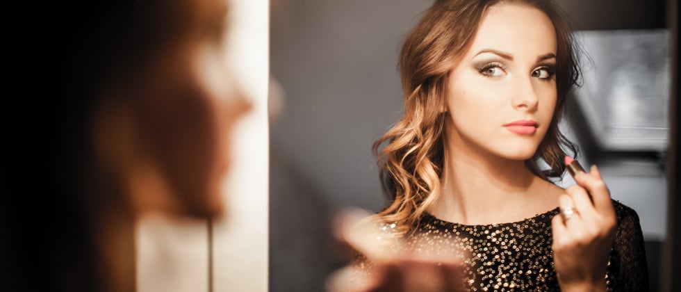 Woman staring at herself in the mirror while putting on lipstick