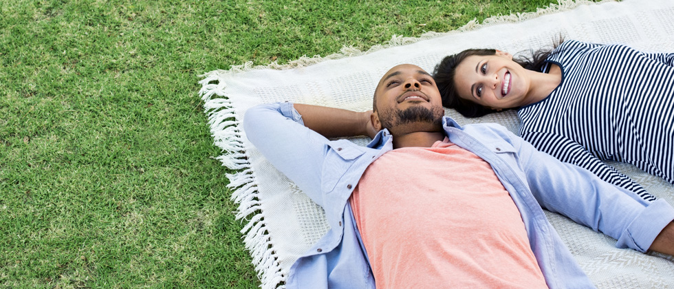 Interracial couple laying together on a picnic blanket in a field