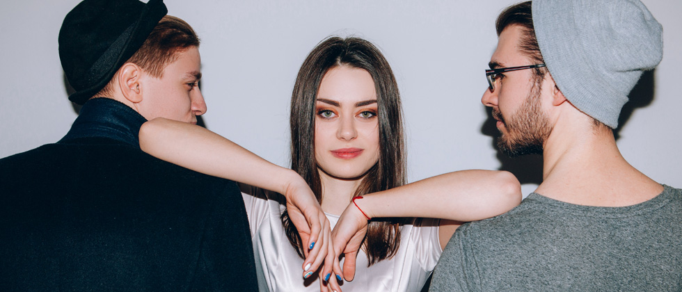 A woman with her elbows on two men's shoulders smirking