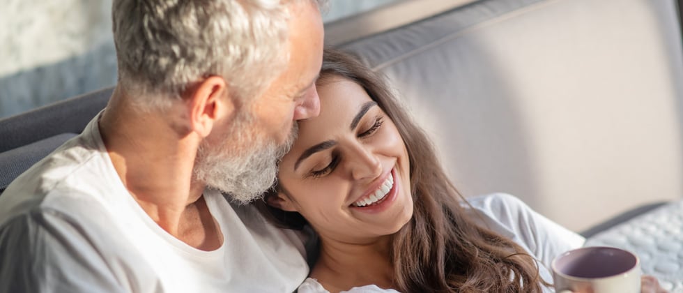 Older man and younger woman cuddling on the couch with coffee