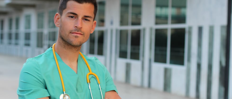 A male nurse standing outside a hospital with his stethoscope