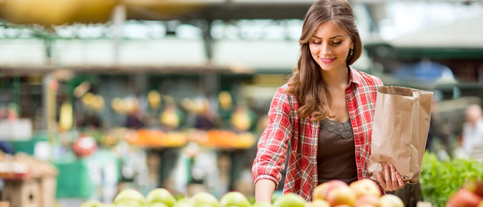 A young woman in the produce aisle picking up groceries