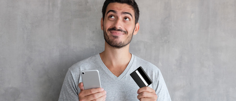 A guy on his phone looking a credit card thinking about buying something