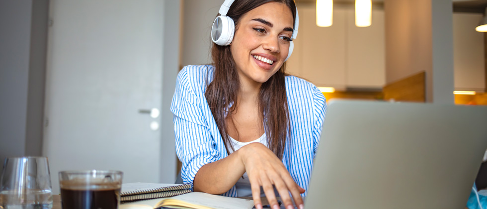 A woman sitting at her laptop with headphones laughing