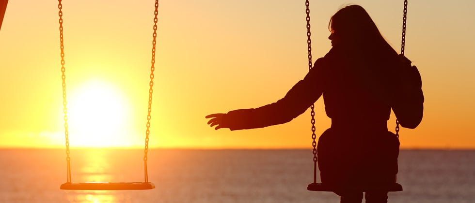 Woman on a swing at sunset reaching for an empty swing next to her