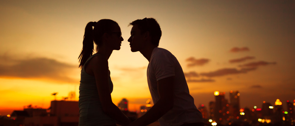 A couple about to kiss at sunset in front of a city scape