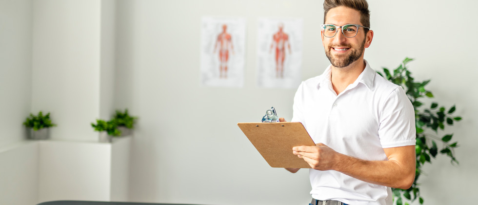A male doctor in his office holding a clipboard and smiling