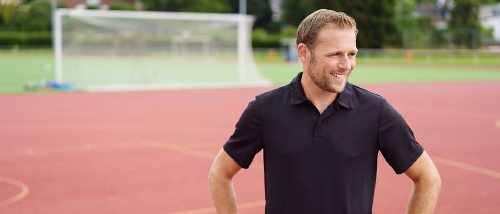 A male coach standing on a track smiling