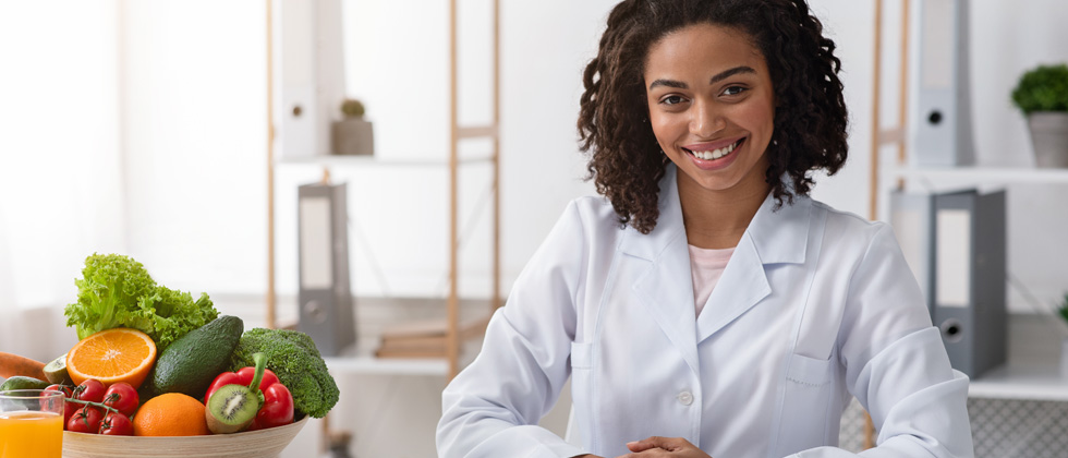 A doctor in a white coat sitting next to a bowl of fruit