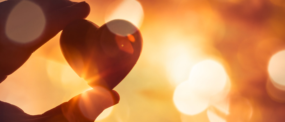 A small heart between two fingers reflecting into the sunlight