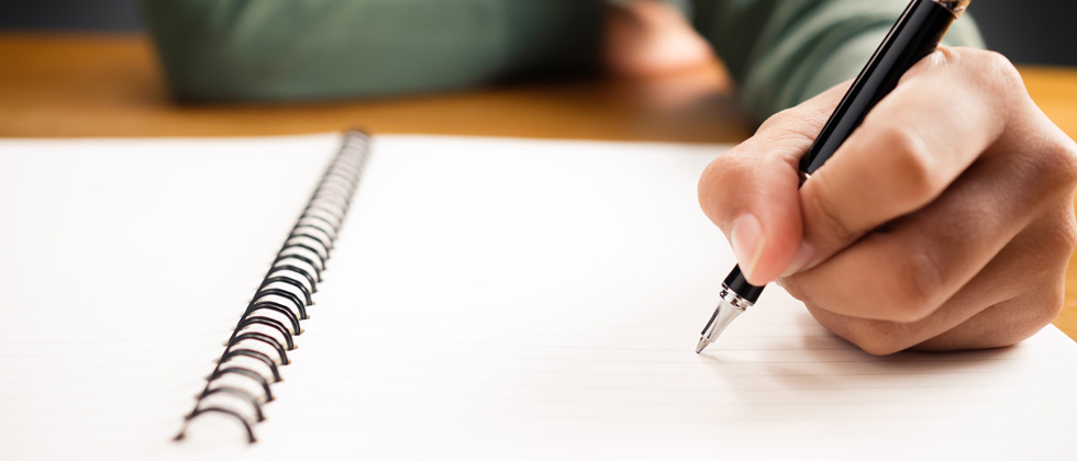 Someone writing in a notebook with their left hand
