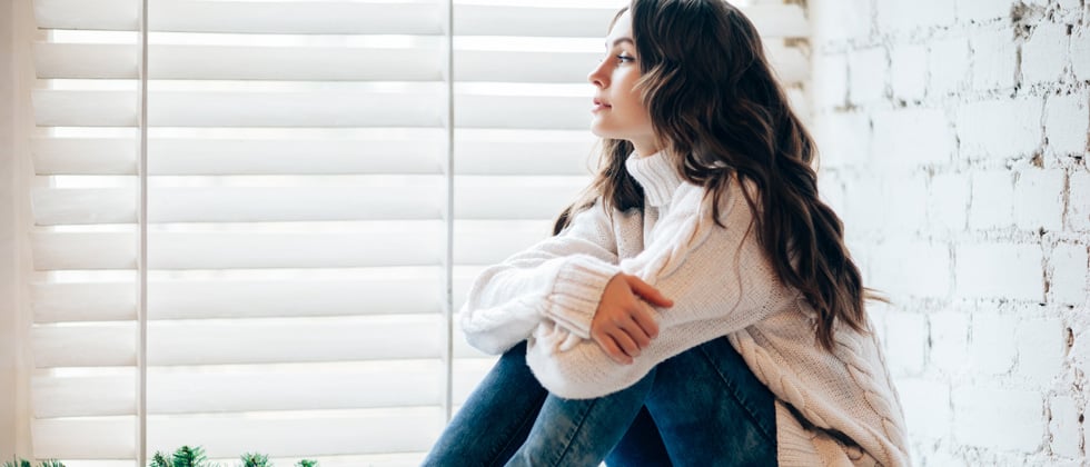 Woman sitting with her knees to her chest looking off thinking