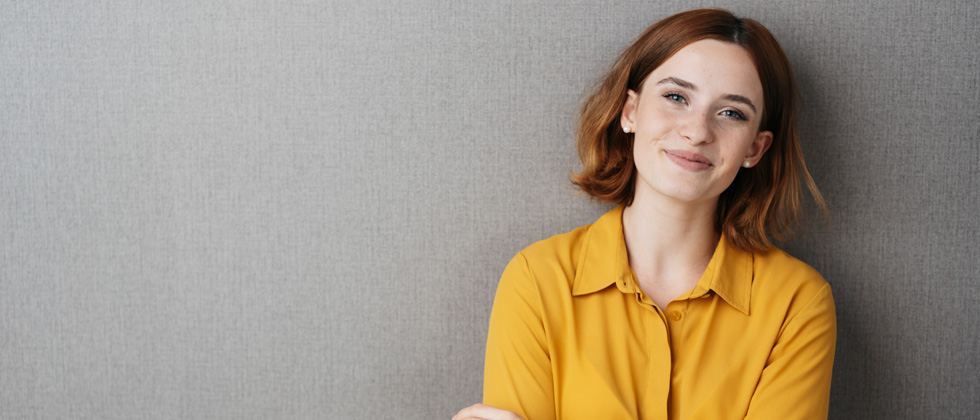 A woman standing and smiling into the camera in a yellow shirt