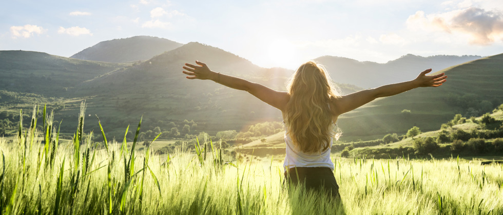 A woman standing in th middle of an open field with her arms open wide