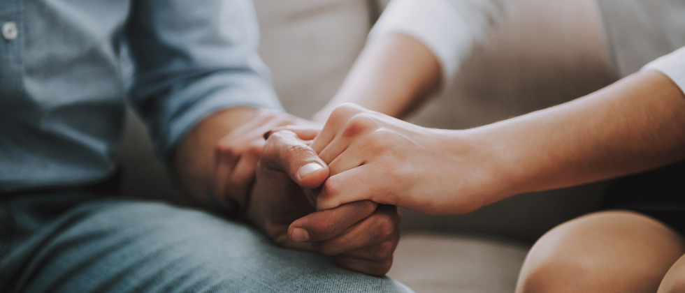 Couple sitting together gripping each other's hands tightly