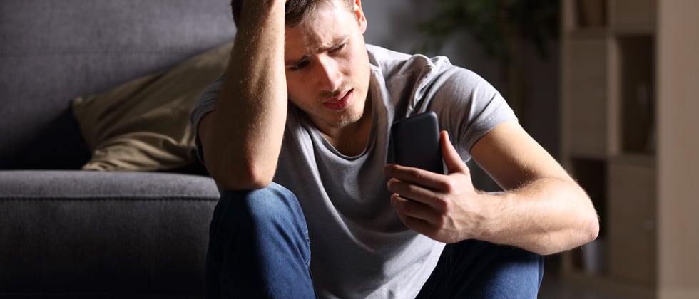 Worried and upset man sitting on the ground looking at his phone