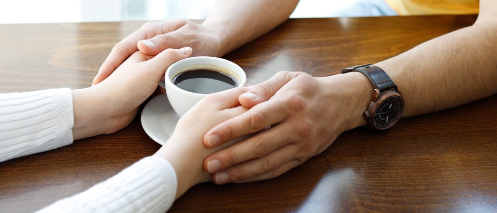 A woman holding her coffee with her boyfriend's hands around hers