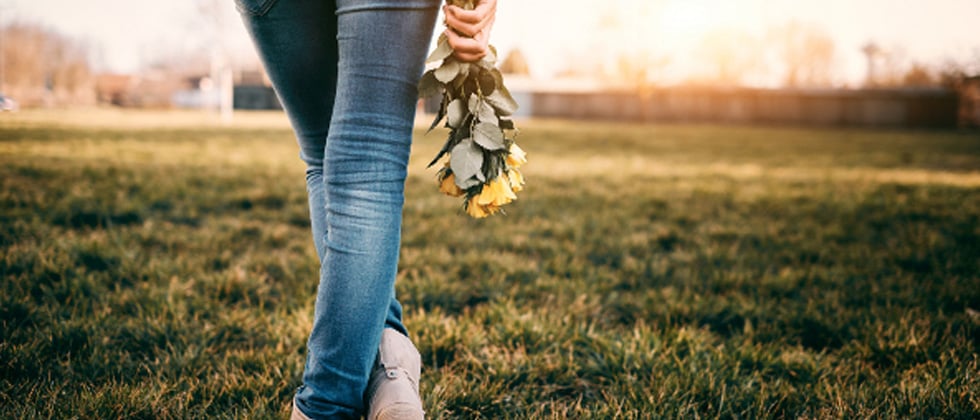 Someone walking in an empty grass field holding yellow roses