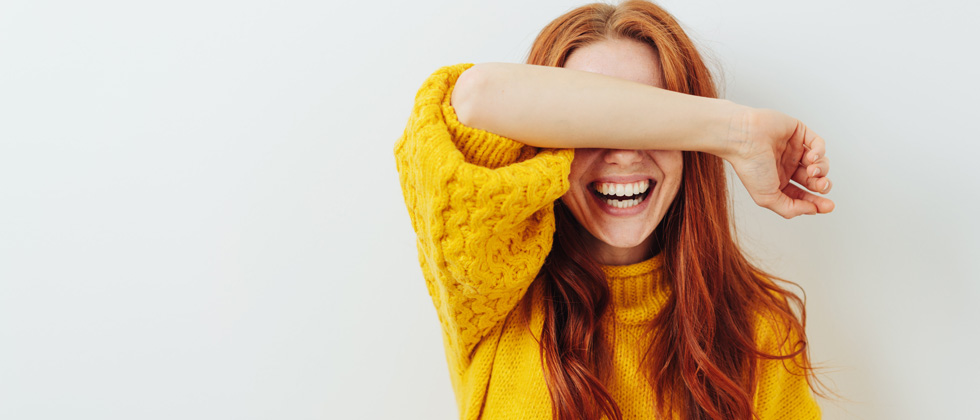 A redhaired woman laughing so hard she's covering her eyes
