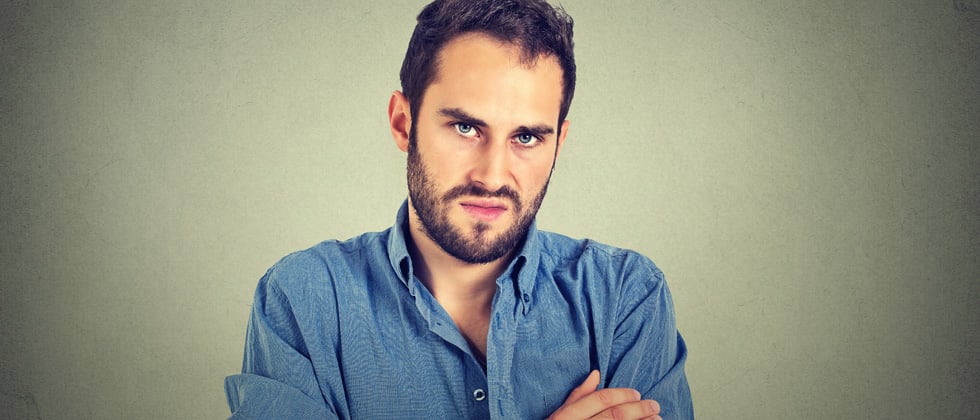 A man with his arms crossed looking irritated into the camera