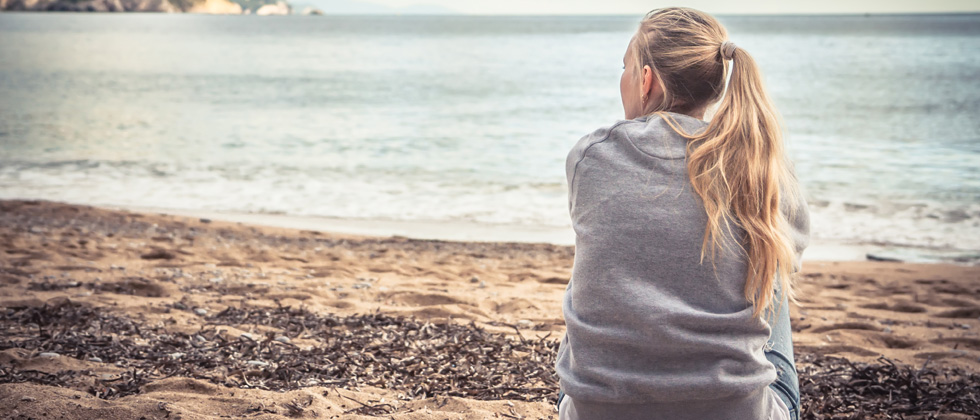 A woman sitting on the beach staring in the ocean