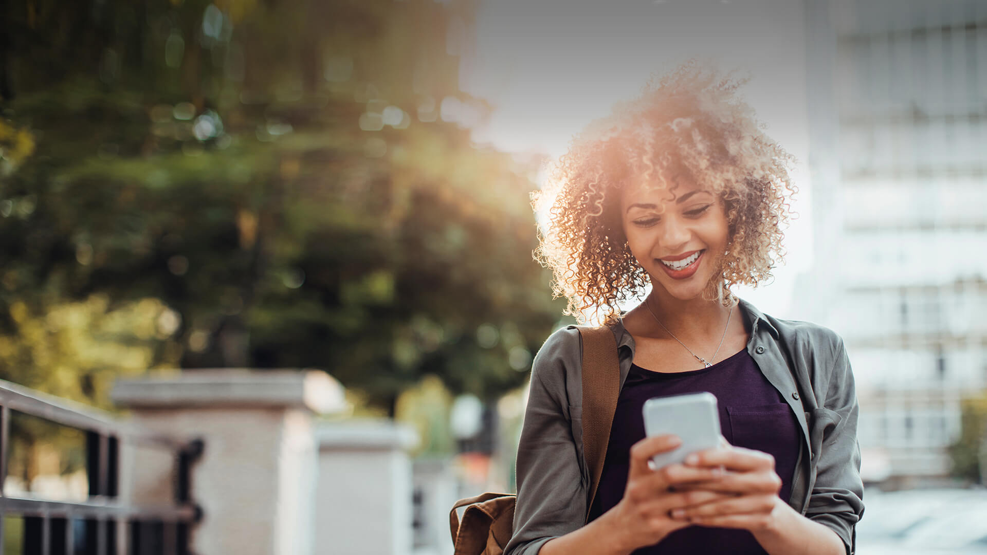 Black single woman smiles in her smartphone while dating online on the go