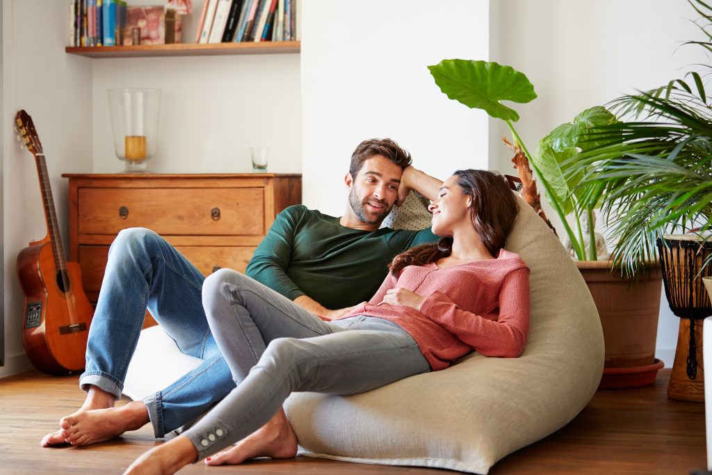 Couple relaxing on a bean bag in the living room talking to each other.