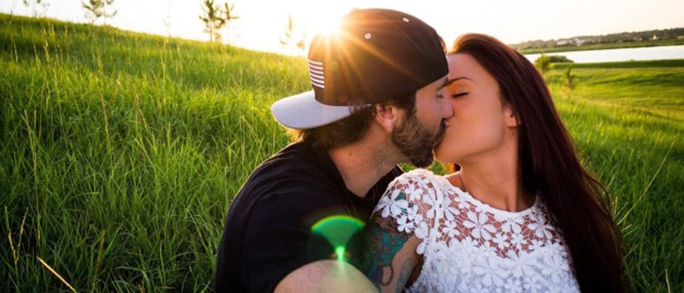 A couple kissing in the middle of a green field