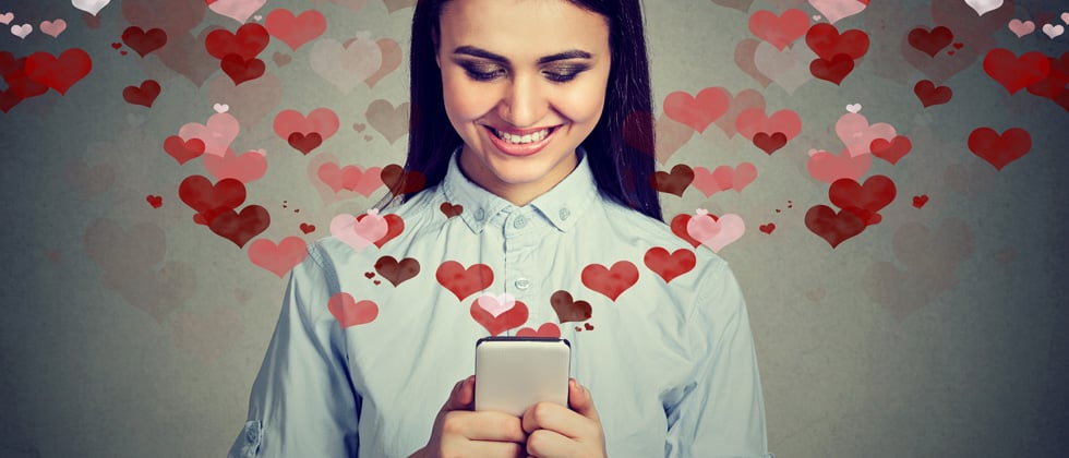 A woman smiling & holding her phone with dozens of hearts flying out of it