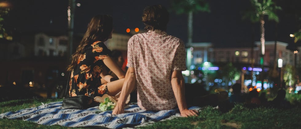 A young couple sitting on a picnic blanket in the park at night