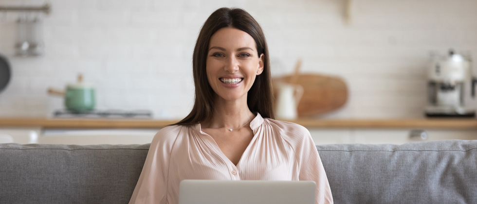 A woman smiling at the camera with her laptop on her lap
