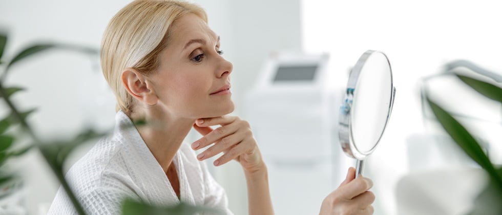A woman looking into a hand held magnifying mirror