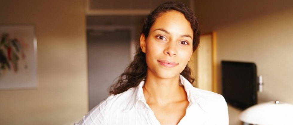 Questions to ask yourself illustrated by a woman standing in her apartment slightly smiling into the camera