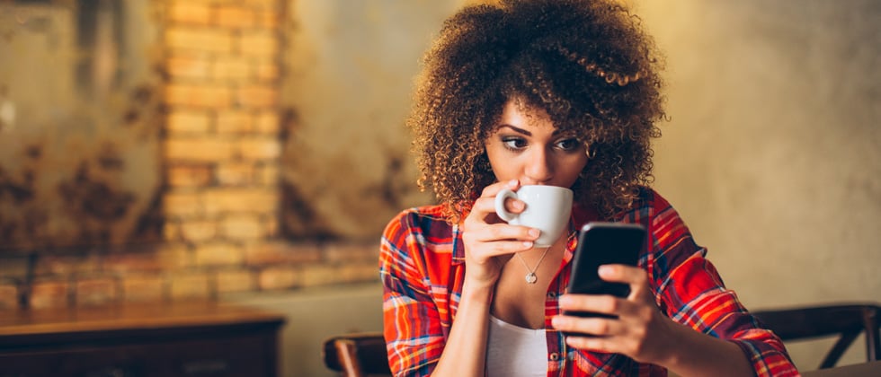 A woman sipping coffee and starring at her phone