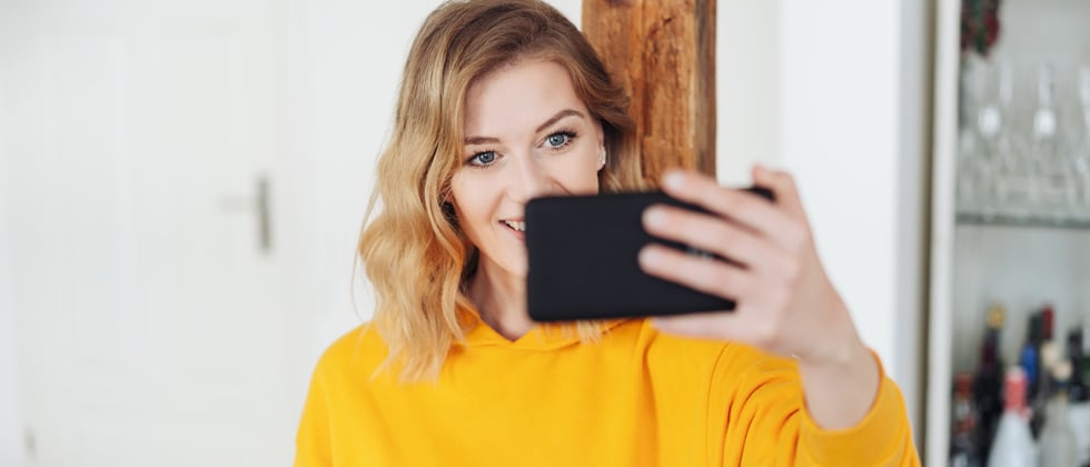 A woman holding up her cell phone taking a cute selfie