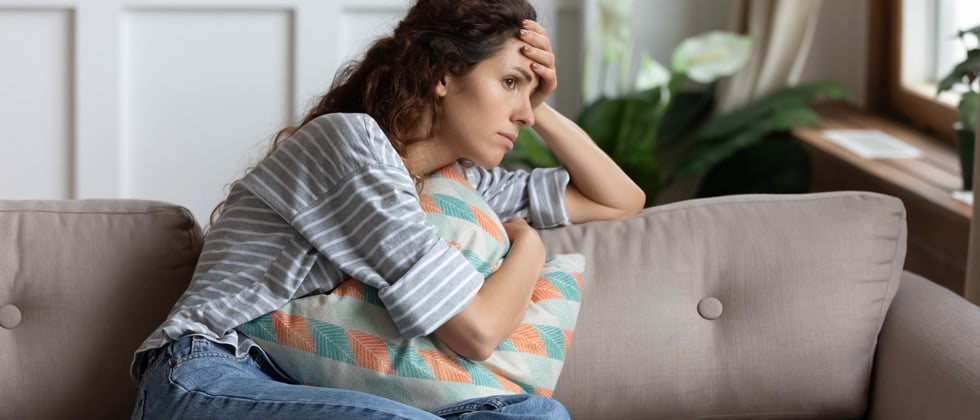 Concerned woman sitting alone on the couch holding a pillow