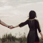 Couple in a field holding hands but walking away from each other