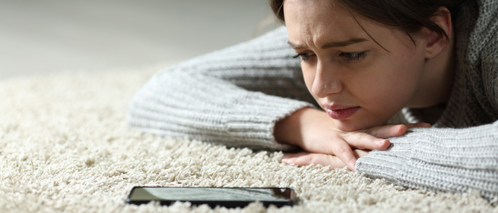 A woman laying on the ground looking upset at her phone