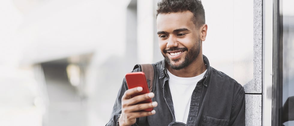 Young man leaning against a wall and smiling at his phone