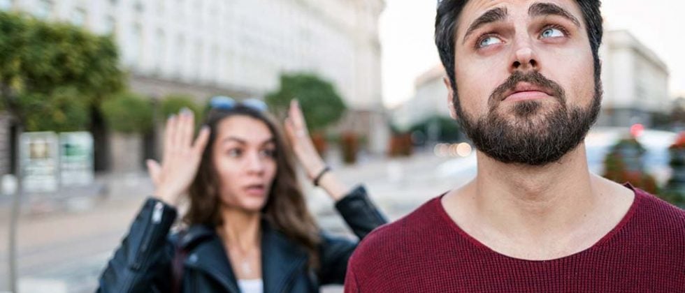 A woman and a man are standing on the street and seem to argue. The woman is looking angry and the man is annoyed.